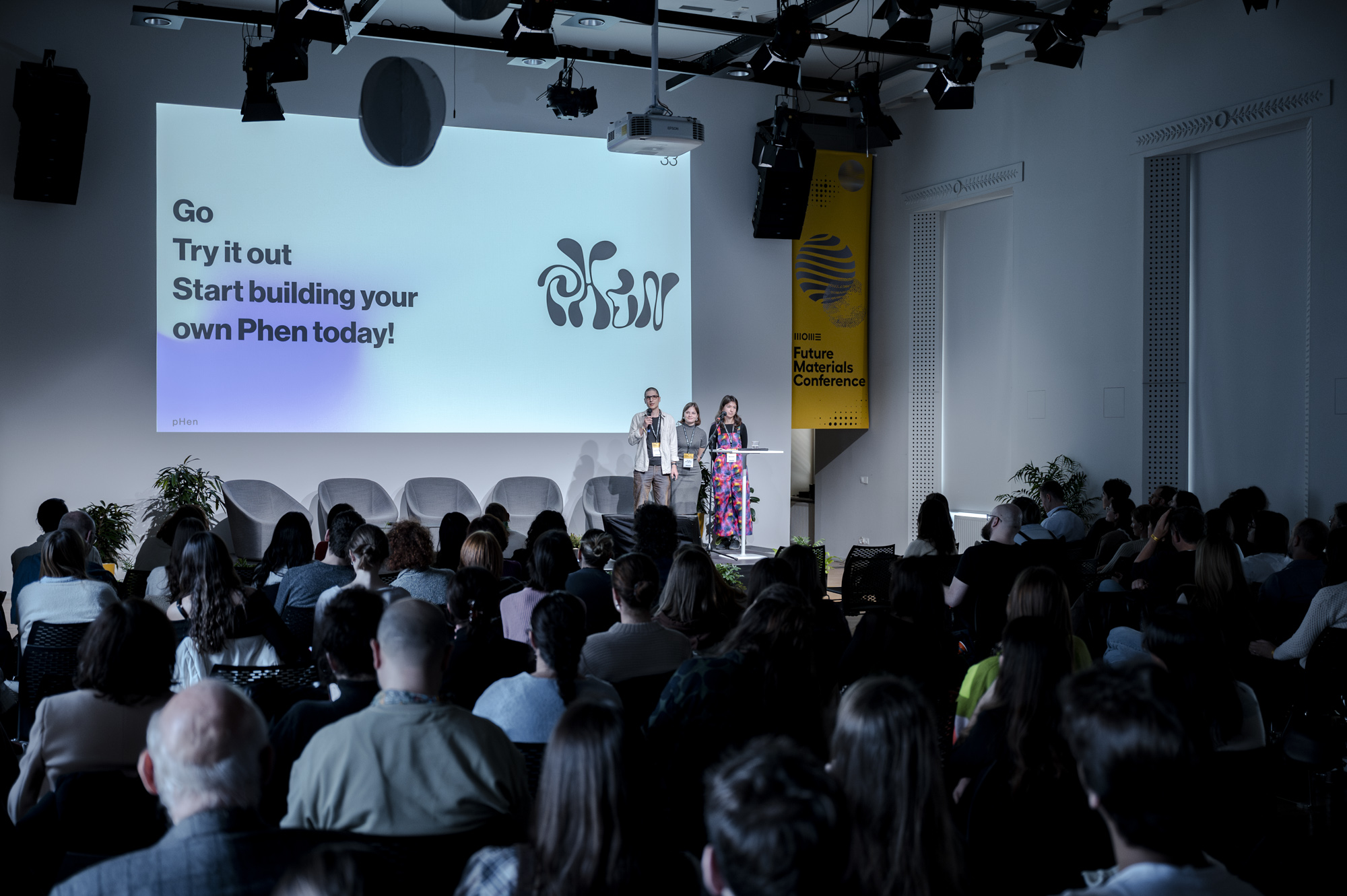 The team of pHen prsenting in front of a large audience. There is a projected prsentation in the background with the pHen logo.